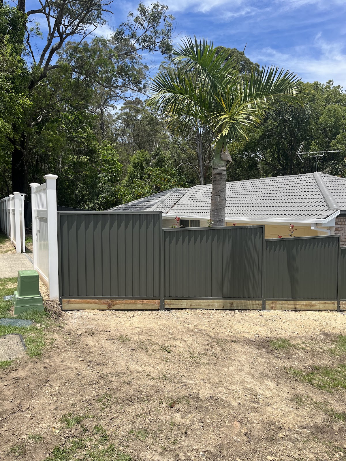 Khaki steel fence stepped on sleepers across a front yard