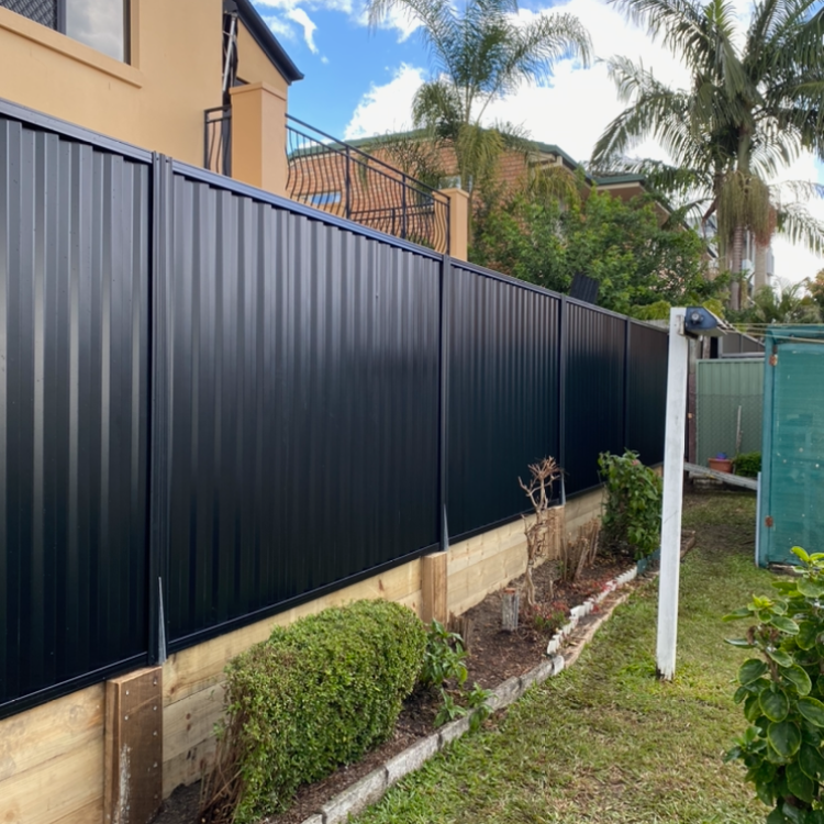 Black Colorbond fence on a timber sleeper plinth along a garden bed